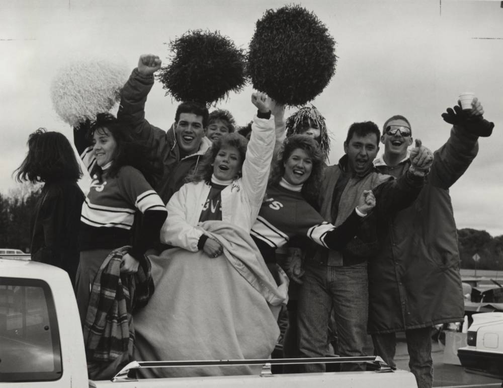 Students standing in the bed of a truck, cheering.